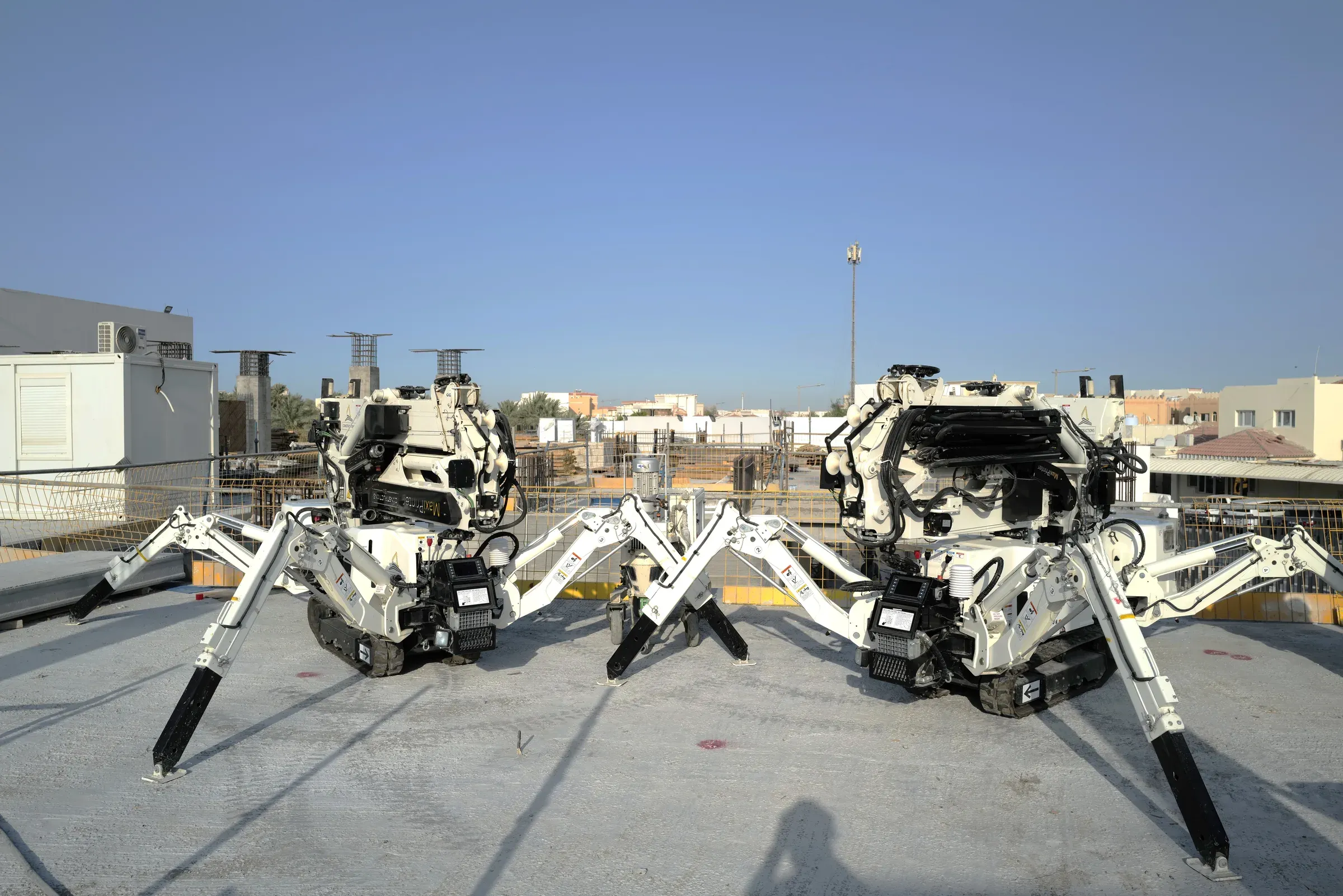 Two 3D printers standing on their legs on the roof slab at School 08, Doha