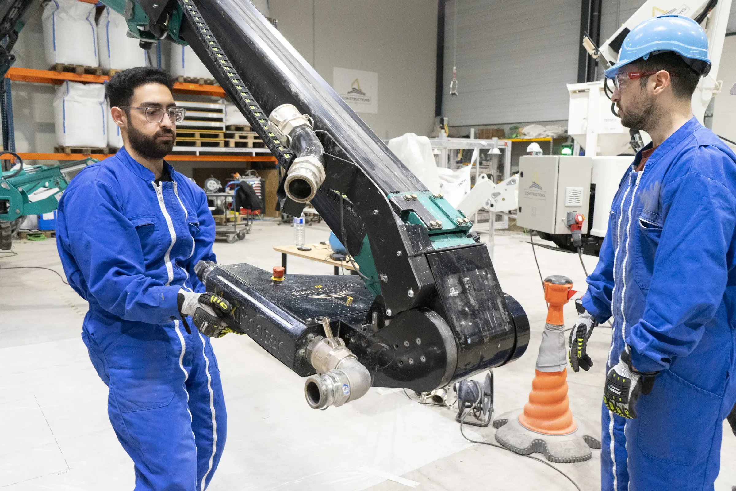 Two GGI team members in blue overalls guiding the printer arm in a workshop