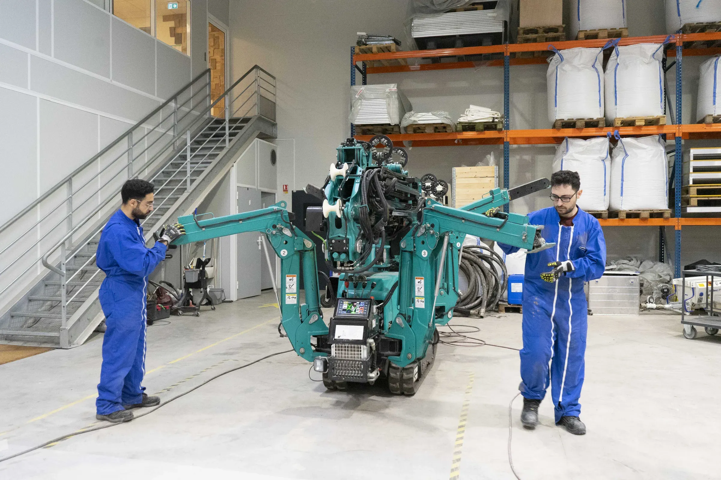 Two GGI operators in blue overalls with a 3D printer in a workshop