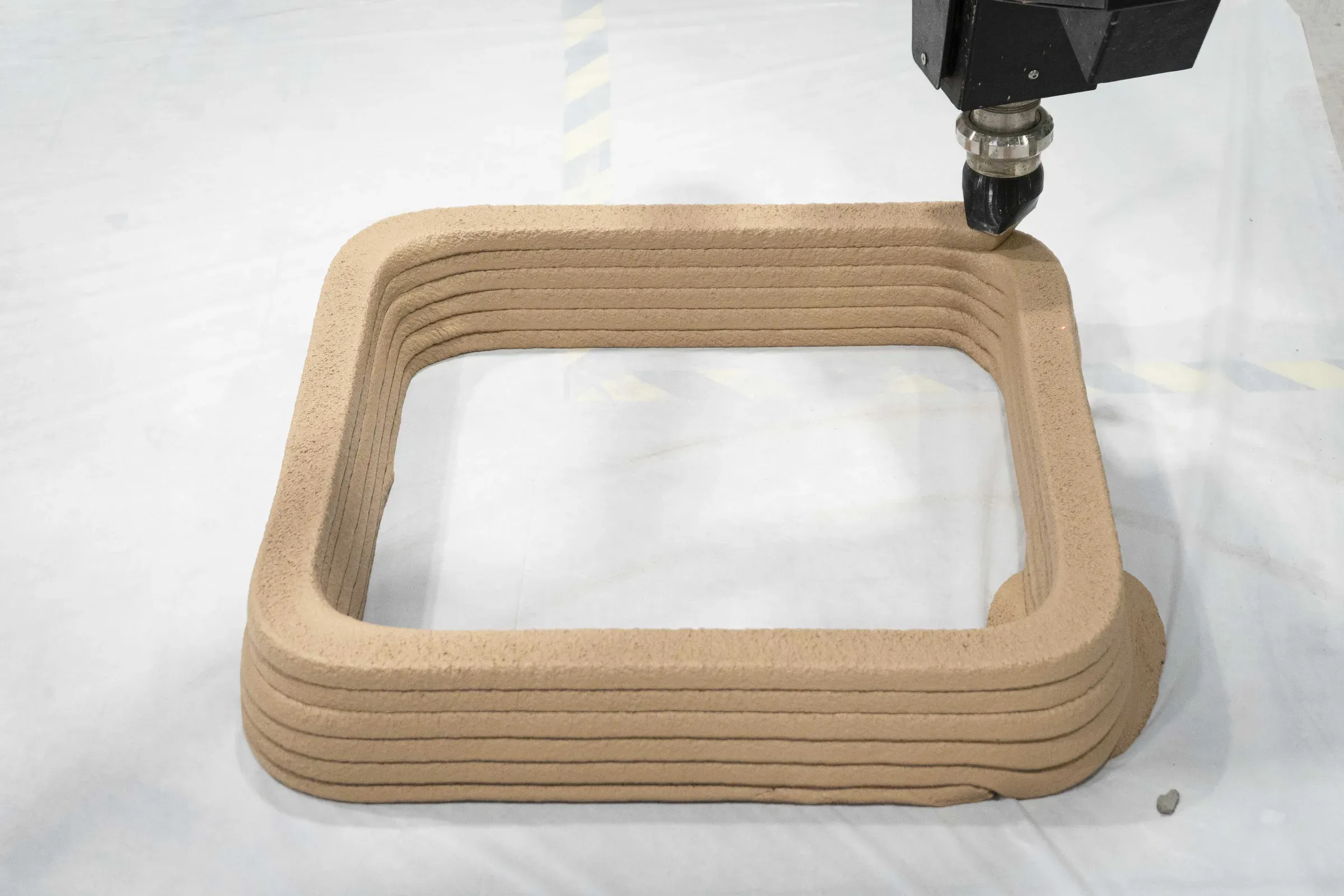A small rectangular test print in clay, its layers laid by the printer nozzle