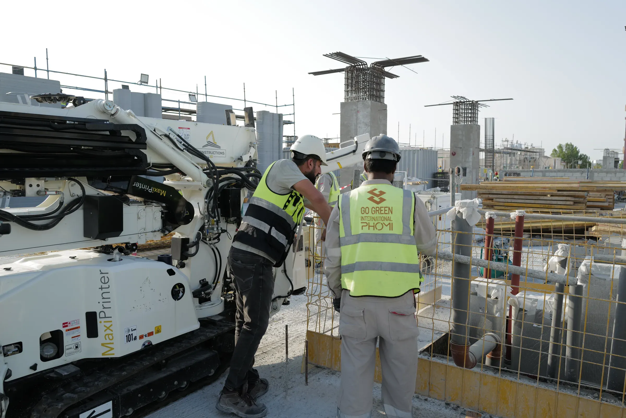 Two GGI crew members in hi-vis vests working at a printer at School 08, Doha