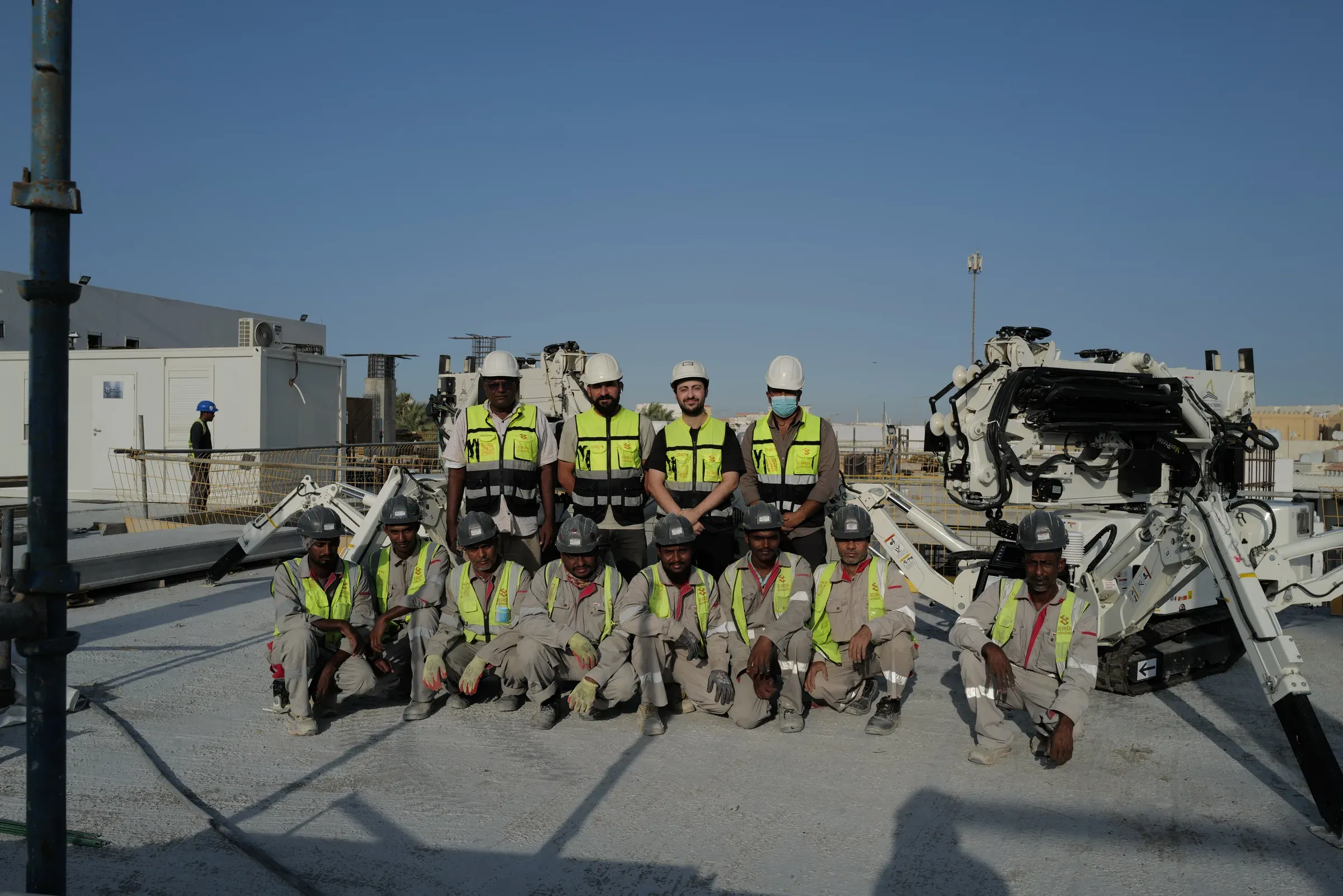 The School 08 printing team standing and kneeling between the two printers on the roof slab, Doha